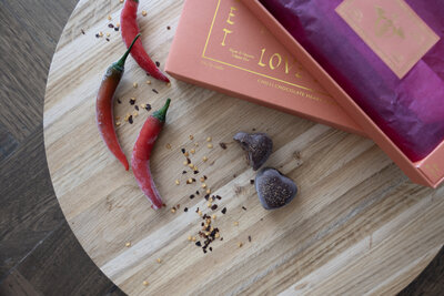 Loco Love Chocolate chill heart truffle on wooden board with chilli flakes , colourful box on Turkish rug in  pink orange and purples