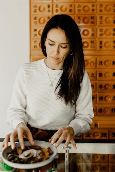 Hands scooping dried herbs into a bowl for tea preparation, symbolizing natural immune support and wellness through traditional chinese medicine