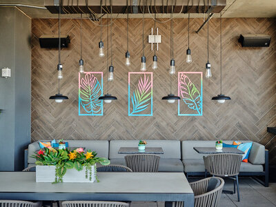 A rooftop terrace with palm leaf neon art, a couch and chairs for guests to eat and drink
