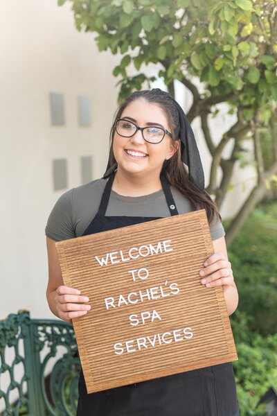 Rachel Smith of Rachel's Spa Services outside spa holding a welcome sign in Boardman, Ohio.