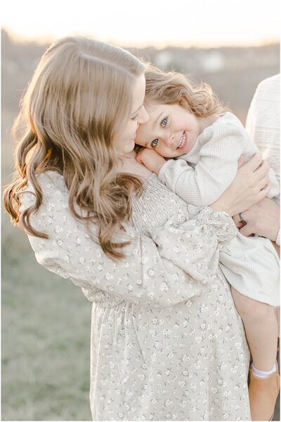 Little girl hugging her mom and smiling at the camera for family photograph