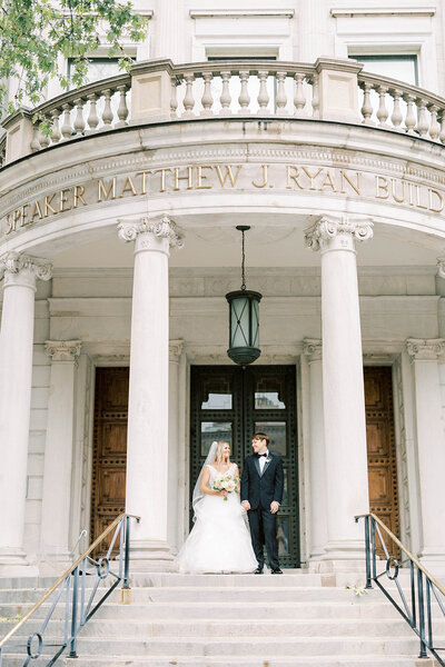 Far away shot of bride and groom standing outside the Speaker Matthew J Ryan Building in Harrisburg, PA.