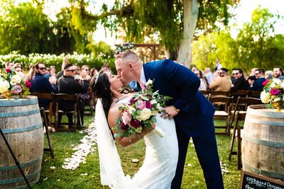 Bride and groom in a dip kissing at the end of the aisle after their wedding ceremony at Galway Downs in Temecula.
