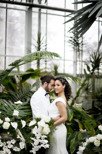 Model wedding couple standing next to greenery inside of greenhouse