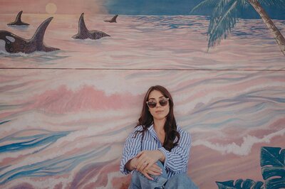 Branding photography of Sharni Tolhurst sitting against a pastel painted mural.