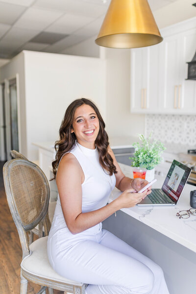 Nashville wedding photographer, Brooke Elliott, editing a wedding in a gorgeous white and gold kitchen with her strawberry acai refresher from starbucks next to her.
