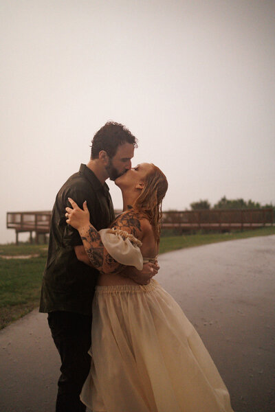 couple kissing in the rain with girl wearing white dress