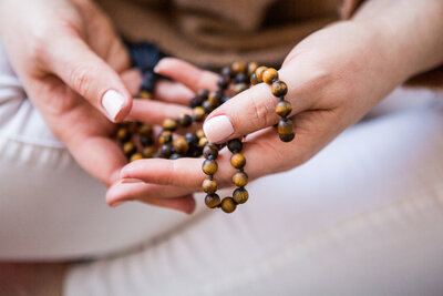 manicured hand holding brown tigers eye mala beads