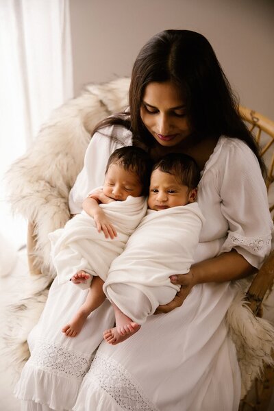 Two twin babies held by their mother and wrapped up in white blankets while photographed by aimee kelly photography in new plymouth
