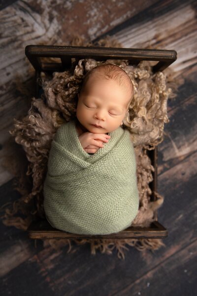 Newborn picture in green swaddle on a newborn bed in brown background in Wellington, FL.
