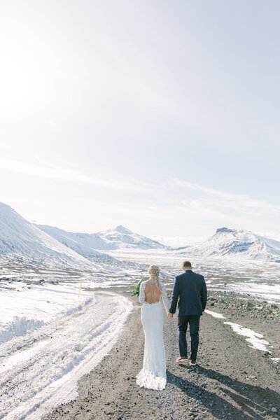 bride and groom in Iceland walking away from the camera with icy mountains in front of them