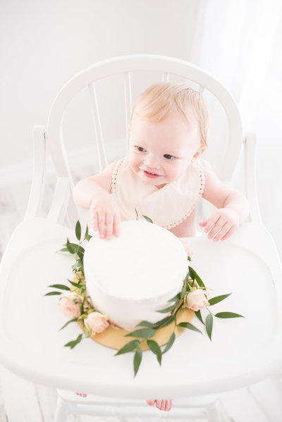 Austin Newborn Photographer Rebecca Dyan headshot sitting in white studio on cream chair wearing a floral dress smiling at the camera