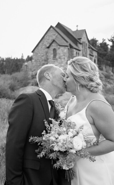 bride and groom kiss in front of chapel on the rock in Rocky Mountain National Park