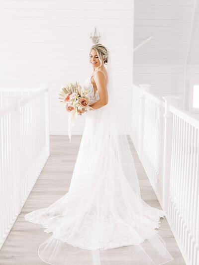 Bride holds her wedding bouquet and looks back over her shoulder while standing on wedding venue balcony