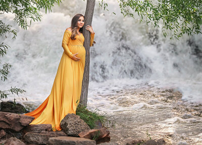 Momma to be posing in yellow dress in front of waterfall