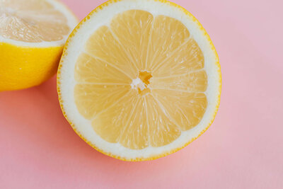 A close-up of two lemon halves placed on a pink background, showcasing their bright yellow flesh and juicy texture.