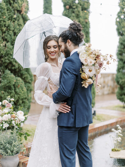bride and groom hugging under an umbrella