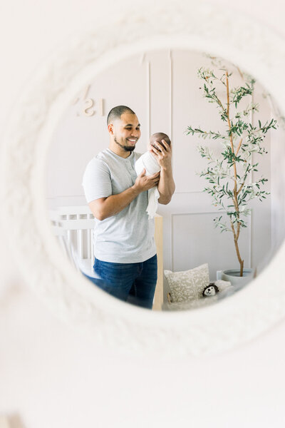 Image of new father holding newborn baby standing next to mirror taken by Newborn Photographer Sacramento Kelsey Krall