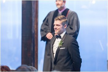 groom watching bride walk down the aisle during wedding ceremony at glassy chapel