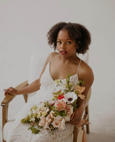 Woman sits in chair and holds a lush bridal bouquet.