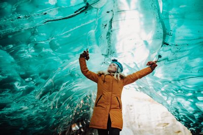 Andi Sweeny wearing a thick orange jacket posing in an ice cave.