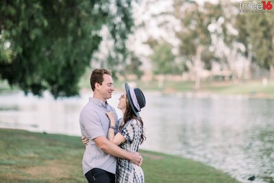 Engaged couple embrace each other in front of the lake at Tri-City Park in Placentia