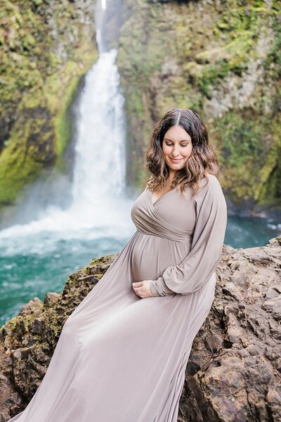 expecting mom in tan dress in front of Wahclella Falls, near Portland, Oregon for maternity photography session with Ann Marshall Photography