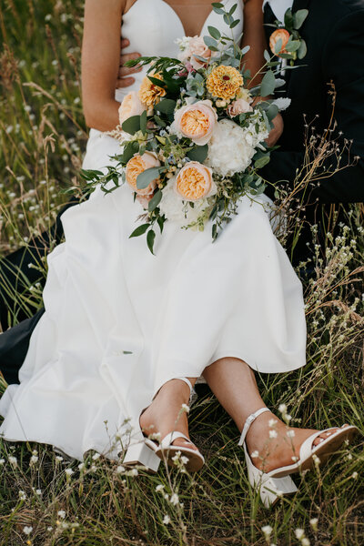 wedding photo of a bride sitting in the grass in her wedding dress with her flowers, taken by Lulle Photo a husband and wife photo and video team based in Mineapolis Minnesota