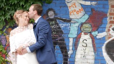 man in suit kissing forehead of woman in wedding dress in front of graffiti art wall