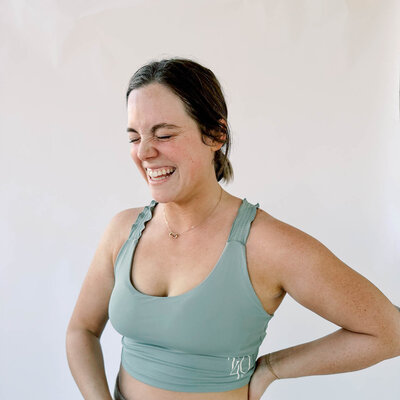 Woman smiling in sage green athletic sports bra with True40 monogram