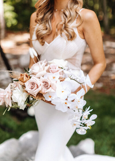 Close photo of bride holding blush roses and white orchid cascade bouquet