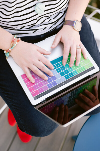 Closeup of  woman's hands typing on a multicolored macbook keyboard - Bloom by bel monili