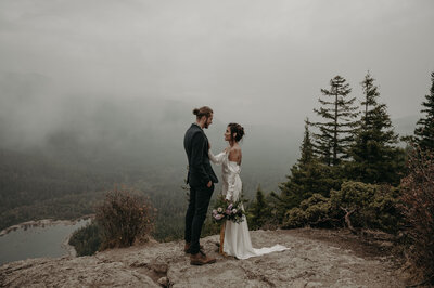 Bride and groom standing on a cliff overlooking the Northern Cascades