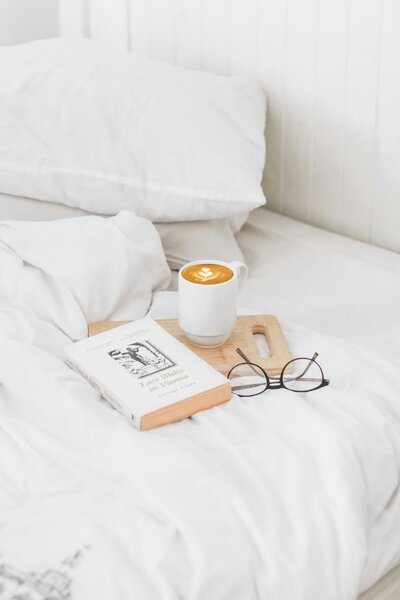 Book and coffee and glasses sitting on cozy bed