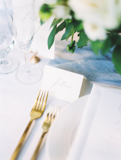 fine art wedding reception place setting with gold flatware and hand lettered place cards