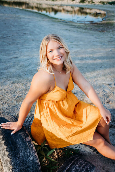 high school senior girl sitting in the grass while wearing a nice dress and glasses