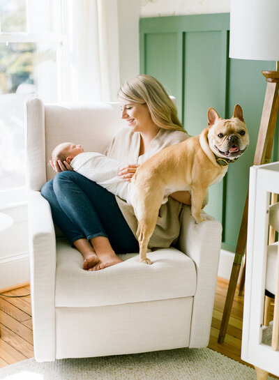 Mom sits in a loungers holding her newborn son with her dog nearby during her lifestyle newborn session in Raleigh NC. Photographed by Raleigh newborn photographers A.J. Dunlap Photography.