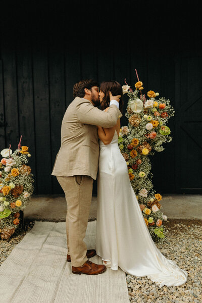 Couple kissing during wedding ceremony in front of black building - New England Wedding Planners