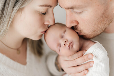 Newborn Baby Boy being kissed by parents on a newborn photoshoot in Cheshire