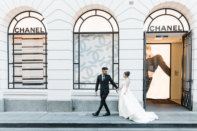 a groom and bride walking in front of a building named chanel with arched windows