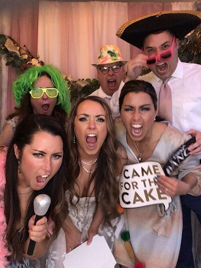 Group of 6 adults in photo booth holding signs and making funny faces at the camera