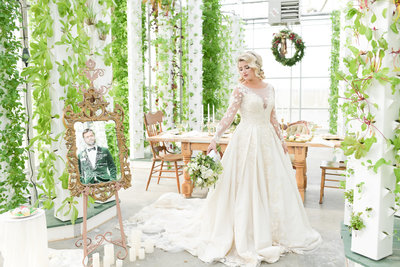 Bride in wedding gown stands in greenery decorated room