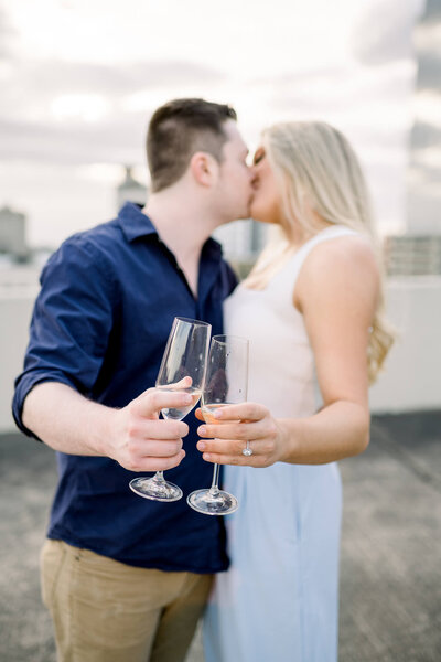 couple kiss atop a parking garage in arkansas while holding champagne glasses in front of themselves