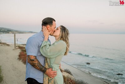 Engaged couple walk along a trail at the Crystal Cove State Beach as they hold hands and laugh during their engagement photo session