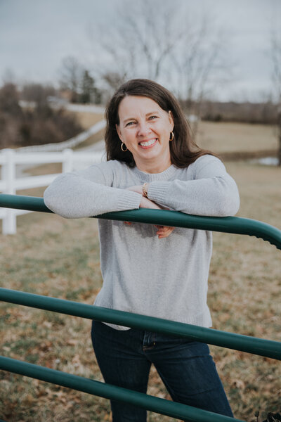 Rachel Sanford in jeans leaning on green farm gate