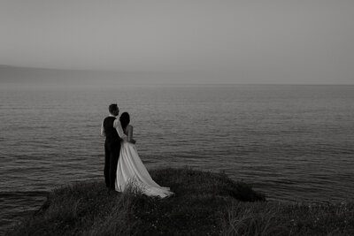 Wedding couple looking out over Atlantic Ocean in Nova Scotia.