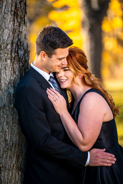 Pittsburgh engagement photography of couple smiling and hugging under a tree at a park near Pittsburgh PA. The couple is lit by flash and dressed in black.