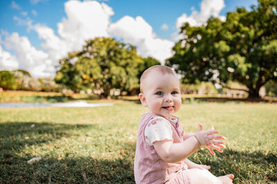 Baby girl sitting in a park clapping her hands - Townsville Milestone Photography by Jamie Simmons