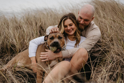 couple and dog sit in grass
