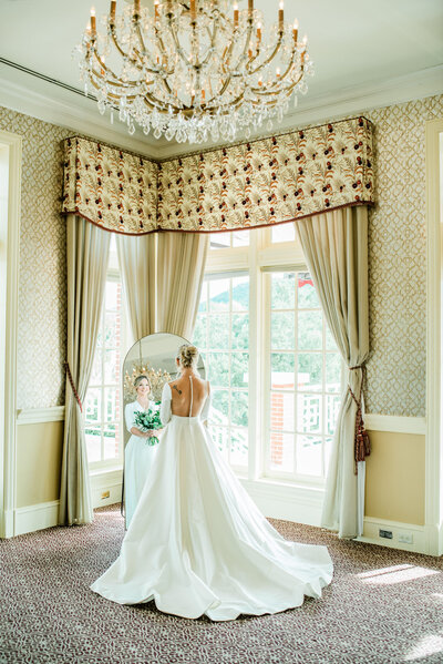 A bride in a elegant princess style wedding dress looks out the window while waiting for her fairytale wedding ceremony to begin on her dream wedding day at Sherwood Country club, a high end wedding venue in California.